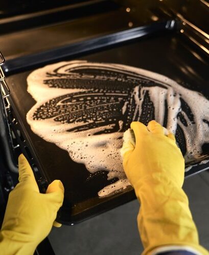 Cleaner's gloved hands performing deep cleaning of the oven